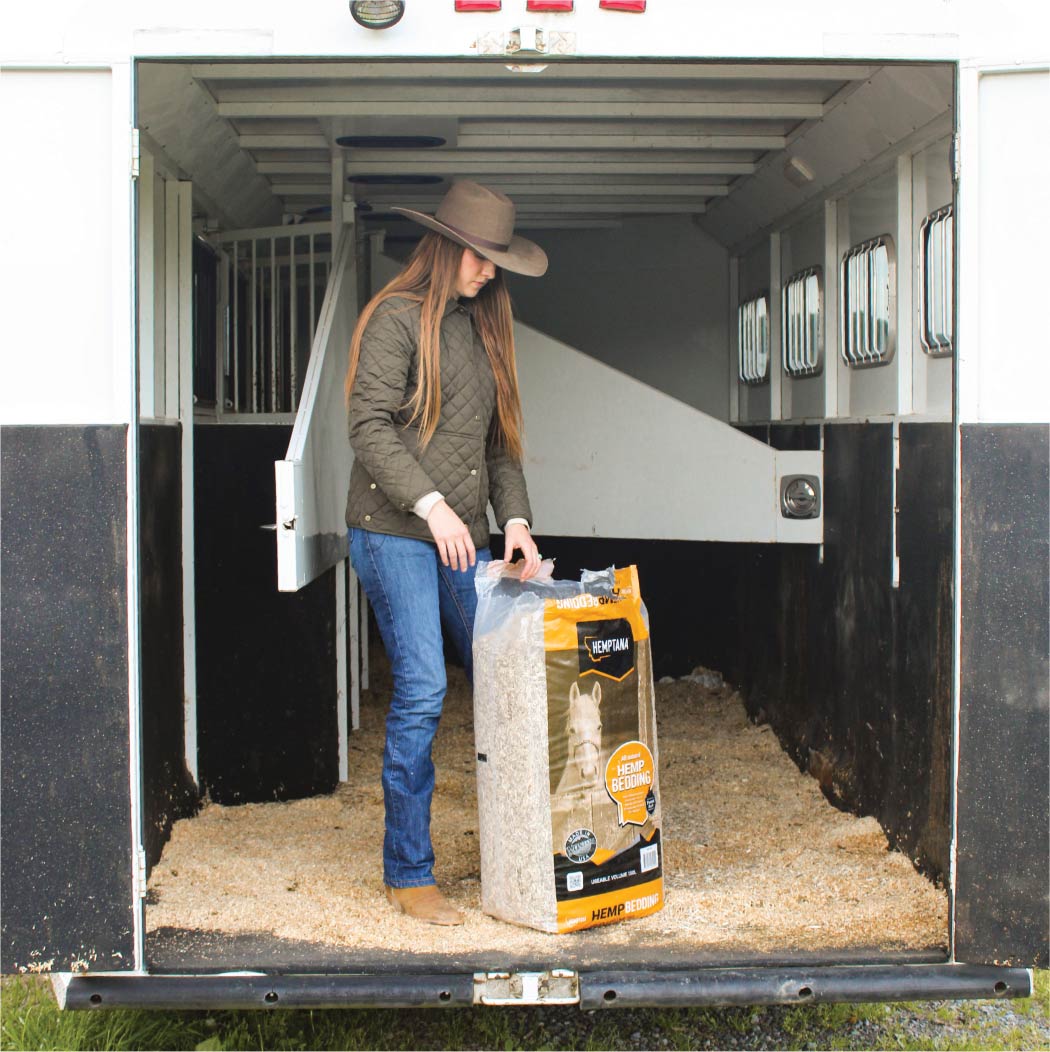 A cowgirl spreading a 70L bag of Hemptana Hemp Bedding in a horse trailer.